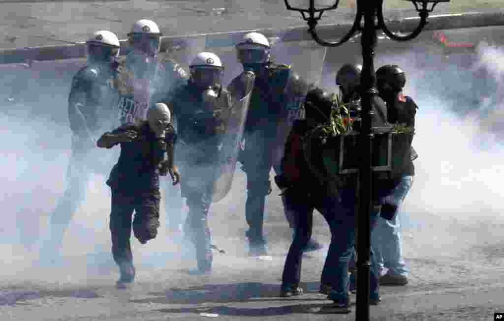 Polisi anti huru-hara mencoba menahan seorang demonstran yang mengenakan masker di tengah-tengah bentrokan di Athena (26/9).