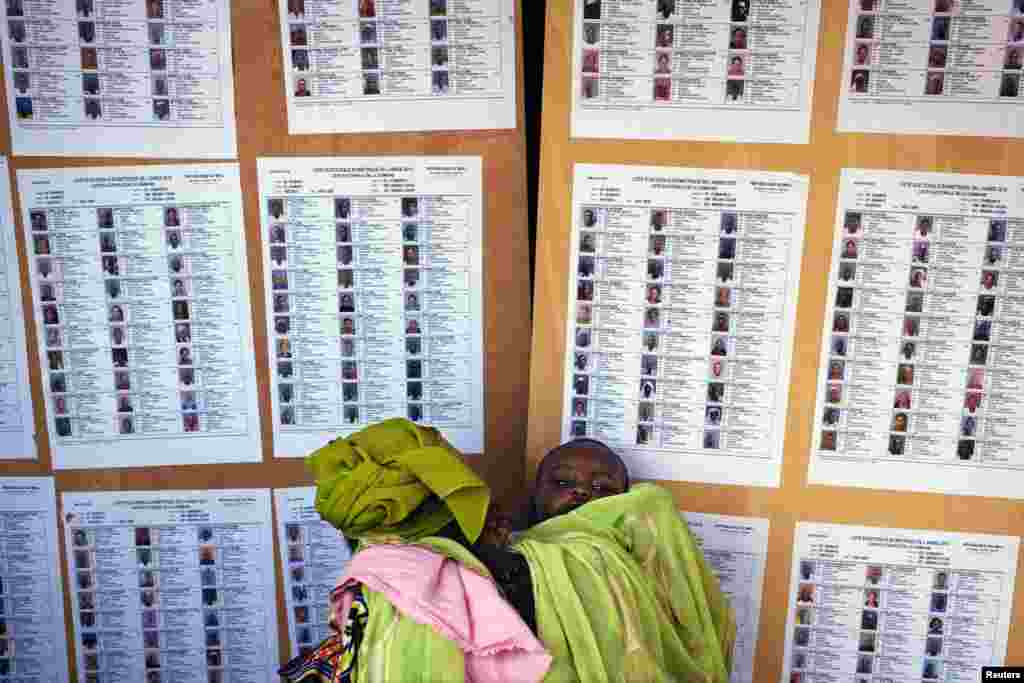 A woman holding a baby searches for her name on a list of eligible voters at an election center in Bamako, Mali.