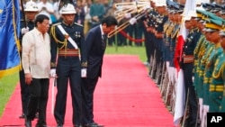 Japanese Prime Minister Shinzo Abe, third from left, escorted by Philippine President Rodrigo Duterte, left, bows to pay respects to national flags during a welcome ceremony at Malacanang Palace grounds, Jan. 12, 2017.