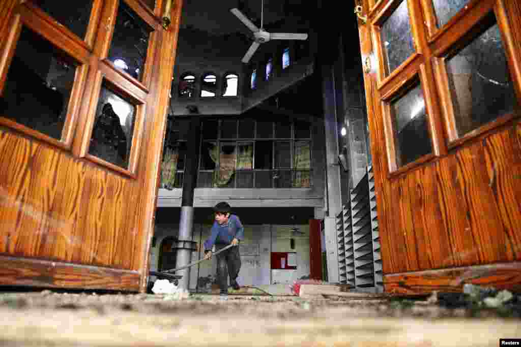 Seorang anak laki-laki membersihkan masjid yang baru terkena serangan udara militer Suriah di distrik Douma, Damaskus.