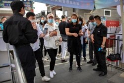 Security guards check the smartphones of people wearing face masks to make sure they have properly registered before being allowed to enter a pedestrian shopping street in Beijing, May 16, 2020.