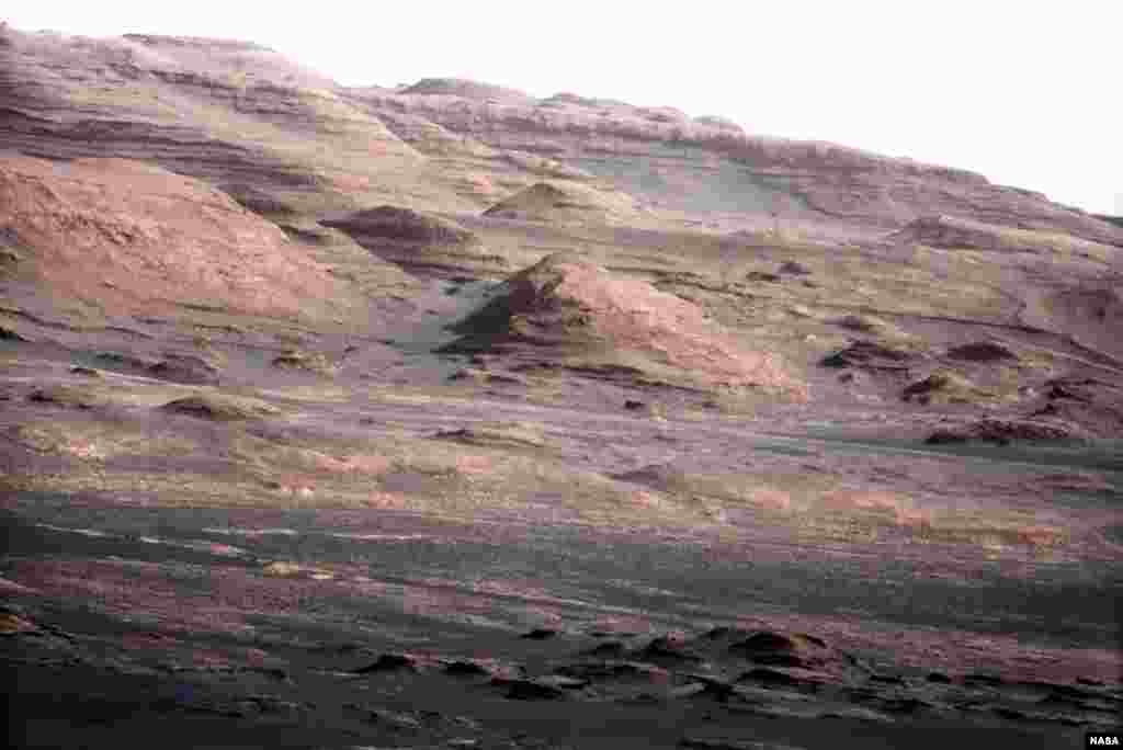 This image shows the base of Mount Sharp, the rover's eventual science destination. Scientists enhanced the color to show the Martian scene under the lighting conditions we have on Earth, which helps in analyzing the terrain.