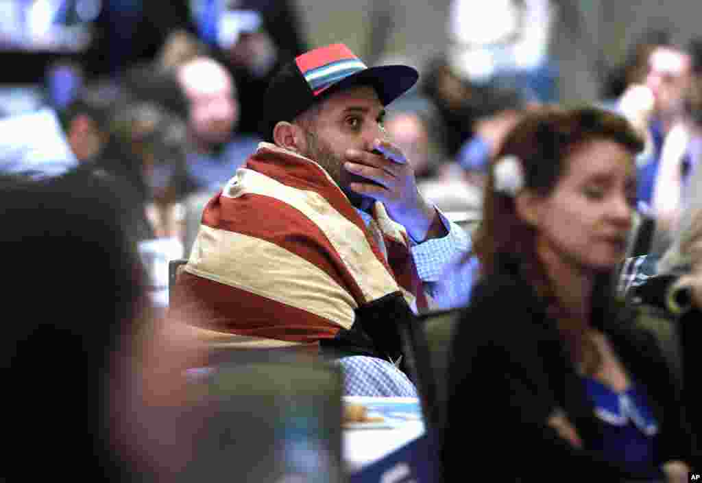 Khaled Nasr dari Boston duduk berselimutkan bendera Amerika saat melihat hasil pemilihan presiden dalam acara nonton bareng di Dallas (8/11). (AP/Tony Gutierrez) 