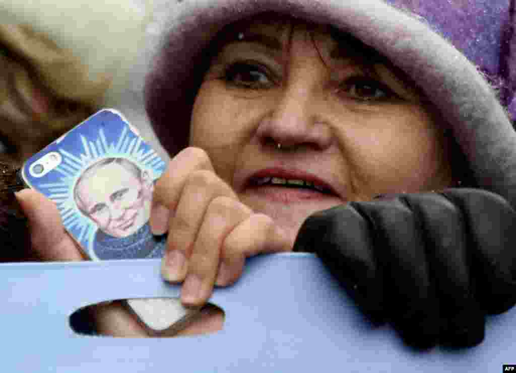 Seorang demonstran pendukung Putin membawa ponsel bergambar Presiden Vladimir Putin dalam aksi unjuk rasa Hari Persatuan Nasional di Moskow.