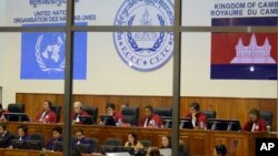 FILE - In this file photo released by the Extraordinary Chambers in the Courts of Cambodia, court officers of the U.N.-backed war crimes tribunal are seen through windows during a hearing of former Khmer Rouge top leaders in Phnom Penh, Cambodia.