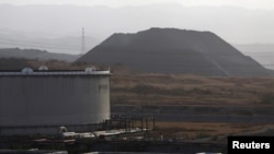 ARCHIVO - Un montículo de coque se ve junto a un tanque de petróleo en el complejo industrial José Antonio Anzoátegui de PDVSA en el estado de Anzoátegui, en Venezuela, el 15 de abril de 2015