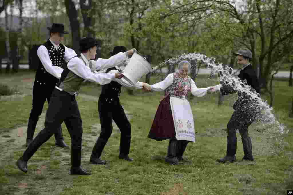 Young men dressed in traditional Paloc folk costumes pour water from a bucket on a young woman performing a folk tradition, the Easter sprinkling, in Kazar, some 100 kilometers northeast of Budapest, Hungary, Good Friday, April 18, 2014. 