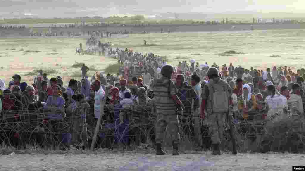 Turkish soldiers stand guard as Syrians wait behind the border fences near the southeastern town of Suruc in Sanliurfa province, Sept. 18, 2014.