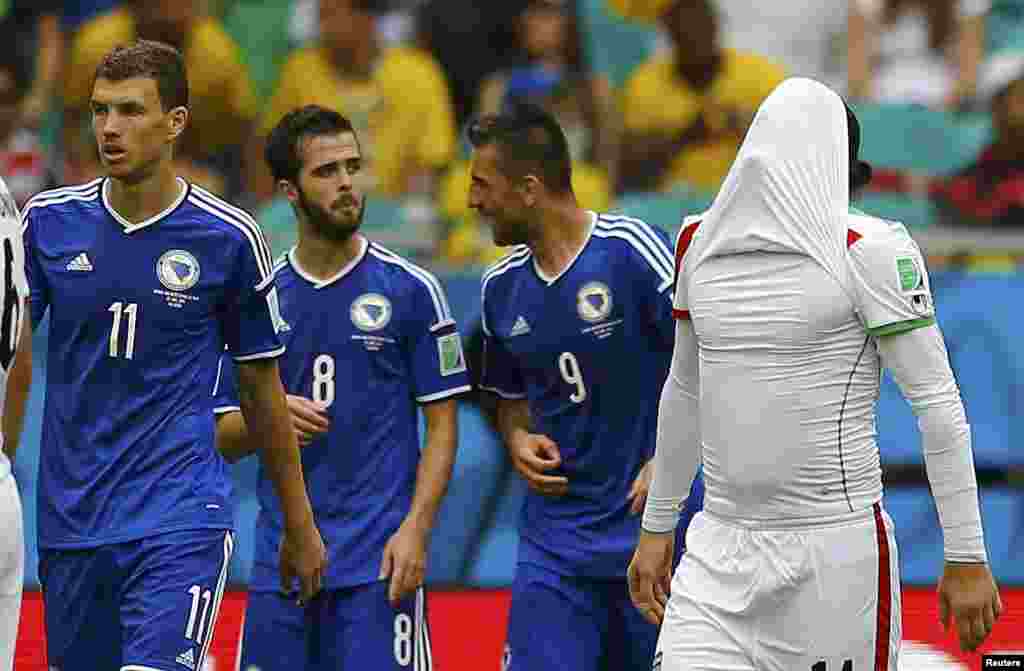 Iranian Andranik Teymourian covers his face as Bosnians Edin Dzeko, Miralem Pjanic and Vedad Ibisevic celebrate their team's second goal at the Fonte Nova arena, in Salvador, June 25, 2014.