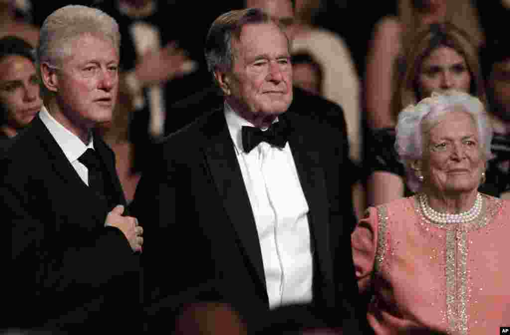 FILE- In this March 21, 2011, file photo, from left, former President Bill Clinton, former President George H.W. Bush and his wife Barbara Bush stand for the National Anthem at the Kennedy Center.