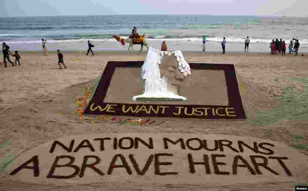 People walk near a sand sculpture with the words "We Want Justice" created by Indian sand artist Sudarshan Patnaik, in solidarity with a gang rape victim who was assaulted in New Delhi, on a beach in the eastern Indian state of Odisha, December 29, 2012.