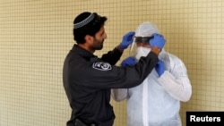 An Israeli police officer helps a Health Ministry inspector put on protective gear before they go up to the apartment of a person in self-quarantine as a precaution against the coronavirus spread, in Hadera, Israel, March 16, 2020.
