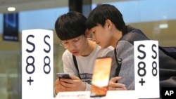 FILE - Students try out a Samsung Electronics Galaxy S8 Plus smartphone at its shop in Seoul, South Korea, April 27, 2017. 