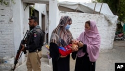 A police officer stands guard as a health worker, right, administers a polio vaccine to a child in a neighborhood of Peshawar, Pakistan, Sept. 9, 2024.
