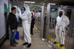 A worker wearing a protective suit takes the temperature of a passenger at the entrance to a subway station in Beijing, China, Jan. 26, 2020.