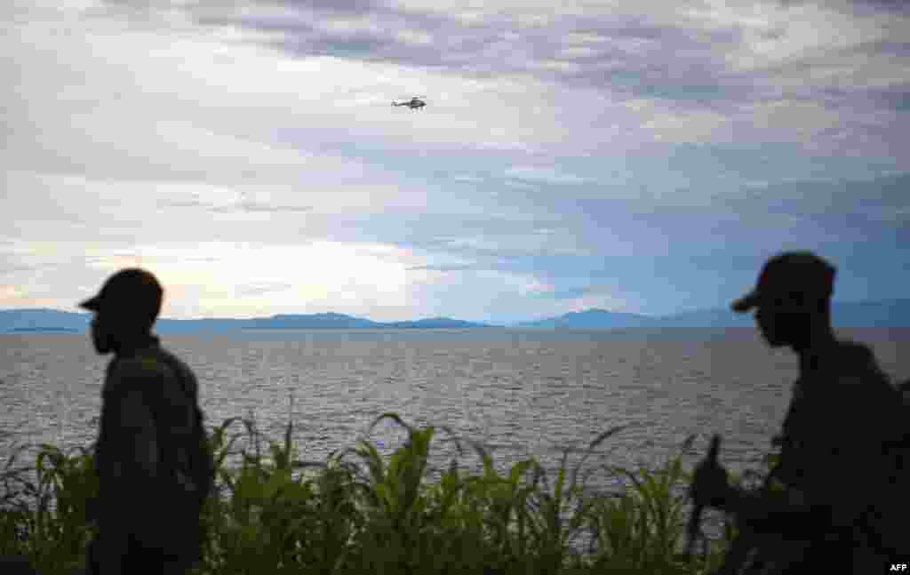 A United Nations helicopter flies over Lake Kivu as M23 rebels walk along the shore in the city of Goma, November 20, 2012.