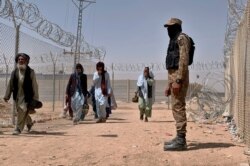 FILE - In this Aug. 20, 2021, file photo, Pakistani army soldier stands guard while Afghan people enter into Pakistan through a border crossing point, in Chaman, Pakistan.