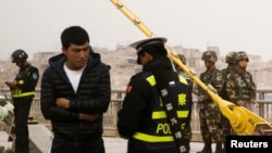 Seorang polisi memeriksa kartu identitas seorang pria sementara pasukan keamanan berjaga di sebuah jalan di Kashgar, Wilayah Otonomi Xinjiang Uighur, China, 24 Maret 2017. 