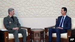 This photo released by the Syrian official news agency SANA, shows Syrian president Bashar Assad, right, meets with Iran's Defense minister Amir Hatami, in Damascus, Aug. 26, 2018. 