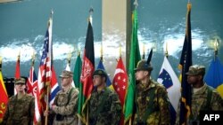 An Afghanistan National Army soldier (C) and ISAF soldiers hold flags during a change of command ceremony at the ISAF headquarters in Kabul on February 10, 2013. 