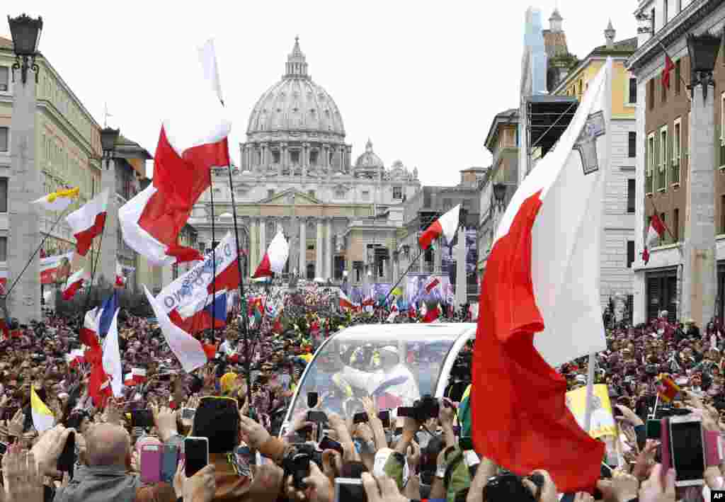 Pope Francis greets the faithful as he is driven through the crowd along Via della Conciliazione while celebrating the ceremony for the canonizations of Pope John XXIII and Pope John Paul II in St. Peter's Square, at the Vatican, April 27, 2014.