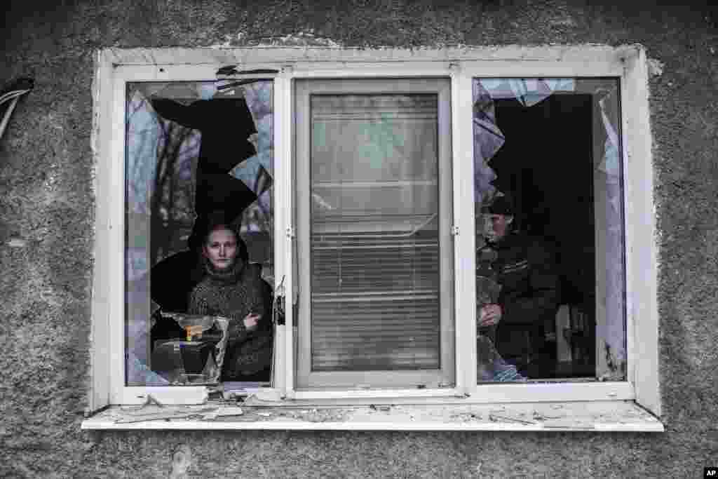 A Ukrainian woman looks through a broken window after it was hit by Ukrainian artillery, near Donetsk, Ukraine, Jan. 18, 2015.