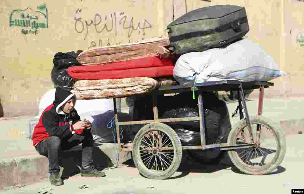 A boy sits next to a trolley containing belongings at the Karaj al-Hajez crossing, Aleppo, Feb. 9, 2014. 