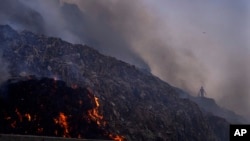 FILE - A person picks through trash for reusable items as a fire rages at the Bhalswa landfill in New Delhi, April 27, 2022. (AP Photo/Manish Swarup, File)