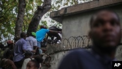 Periodistas se encaraman sobre una pared para evitar disparos de una pandilla en el Hospital General en Puerto Príncipe, el 24 de diciembre del 2024. 