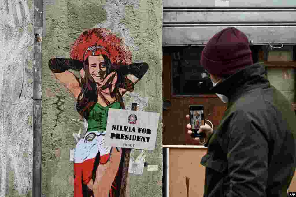 A man takes a photo of a mural entitled "Thank goodness Silvia is here," representing former Italian prime minister and presidential candidate Silvio Berlusconi dressed as a woman, by Italian street artist Salvatore Benintende aka TvBoy, in Milan.