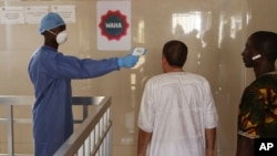 FILE - A health worker, center, takes the temperature of people to see if they might be infected by the Ebola virus inside the Ignace Deen government hospital in Conakry, Guinea, March 18, 2016.