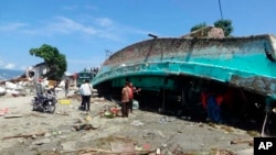 Warga menyaksikan kapal yang terdampar diterjang tsunami di Palu, Sulawesi Tengah, Minggu, 30 September 2018.