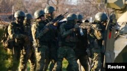 Pria-pria bersenjata, diyakini merupakan tentara Rusia, berlindung di balik tank saat berupaya merebut pangkalan angkatan udara di Belbek, Krimea (22/3).