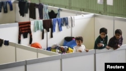 FILE - Children watch as they stand on beds in a shelter for migrants inside a hangar of the former Tempelhof airport in Berlin, Germany, Dec. 9, 2015. 