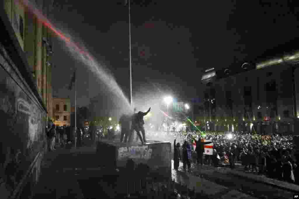 Demonstrators stand atop of a tomb under running water from a water cannon rallying outside the parliament's building to continue protests against the government's decision to suspend negotiations on joining the EU in Tbilisi, Georgia.