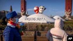 Para warga yang menggunakan masker tampak melihat maskot dari Olimpiade dan Paralimpiade Musim Dingin 2022 yang ditampilkan di dekat arena olahraga di Beijing, pada 12 Januari 2022. (Foto: AP/Mark Schiefelbein)