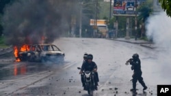 FILE - A police officer aims his gun at two men riding a motorcycle during a protest against Nicaragua's President Daniel Ortega in Managua, May 28, 2018. 