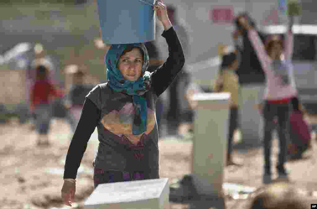Une femme de réfugié kurde syrienne de la région Kobané porte un seau d'eau sur la tête dans un camp de Suruc, près de la frontière Turquie-Syrie lundi 3 novembre 2014.