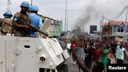 FILE - Residents chant slogans against Congolese President Joseph Kabila as U.N. peacekeepers patrol during demonstrations in the streets of the Democratic Republic of Congo's capital Kinshasa, Dec. 20, 2016.
