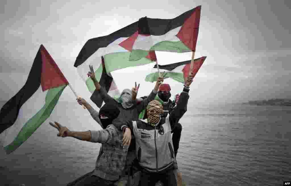 Para pemuda Palestina melambai-lambaikan bendera nasional mereka menjelang peluncuran inisiatif konvoi perahu-perahu kecil yang mereka namakan "Koalisi Pemuda Intifada" untuk mematahkan blokade laut militer Israel atas kota Gaza.