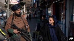 ARCHIVO - Un combatiente talibán monta guardia mientras una mujer pasa caminando en Kabul, Afganistán, el 26 de diciembre de 2022. 