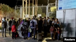 Refugees and migrants stand at the closed gate of the Moria migrant camp, after a fire at the facility, on the island of Lesbos, Greece, Sept. 19, 2016. 