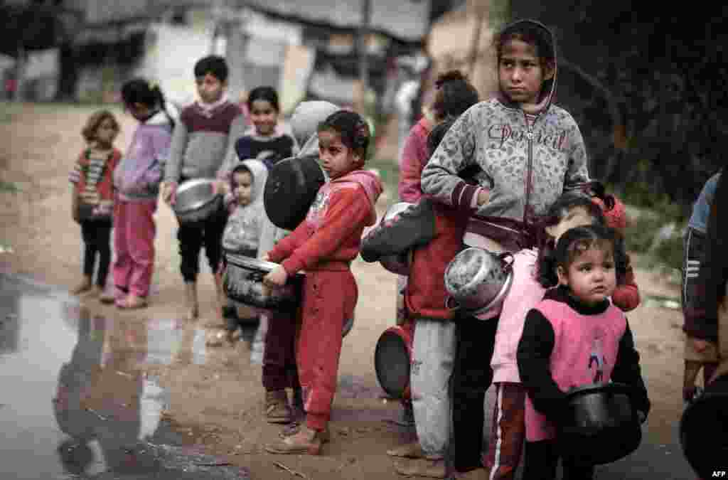 Anak-anak Palestina membawa bejana saat antre untuk menerima bantuan makanan yang disiapkan dengan bahan-bahan yang disumbang oleh para dermawan yang ingin membantu keluarga yang membutuhkan, di lingkungan miskin di Kota Gaza, pada 28 Januari 2021. (Foto: Mahmud Hams / AFP) 
