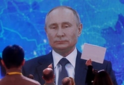 FILE - Journalists sit in front of an electronic screen during Russian President Vladimir Putin's annual end-of-year news conference, held online in a video conference mode, in Moscow, Dec. 17, 2020.
