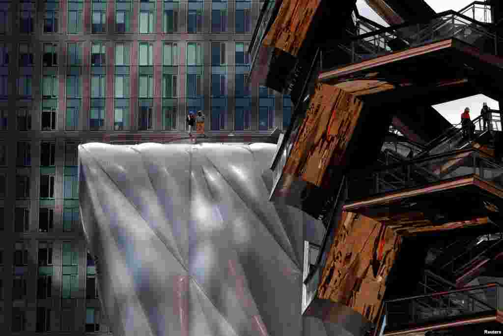 Workers are seen on 'The Vessel' (R) comprised of 154 connected flights of stairs and 80 landings designed by Thomas Heatherwick and on 'The Shed' arts center (L) at the Hudson Yards development on Manhattan's West side, in New York City, New York, U.S., March 12, 2019.