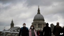 People wearing face masks walk across the Millennium footbridge backdropped by the dome of St Paul's Cathedral in London, March 10, 2020.