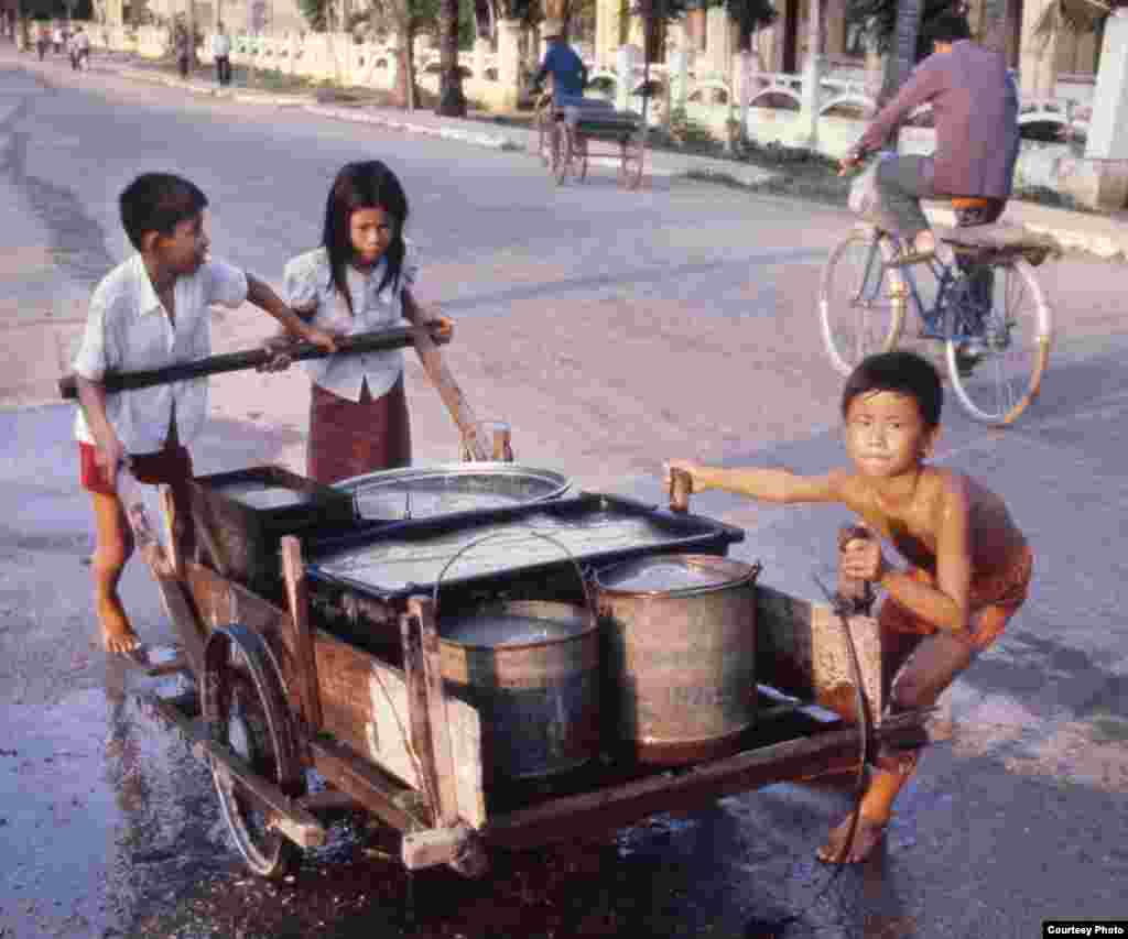 កុមារកម្ពុជាជញ្ជូនទឹកដើម្បីយកទៅប្រើប្រាស់។ រូបភាពថតនៅភ្នំពេញ ក្នុងឆ្នាំ១៩៨០។ (រូបផ្តល់ឱ្យដោយលោក John Burgess)