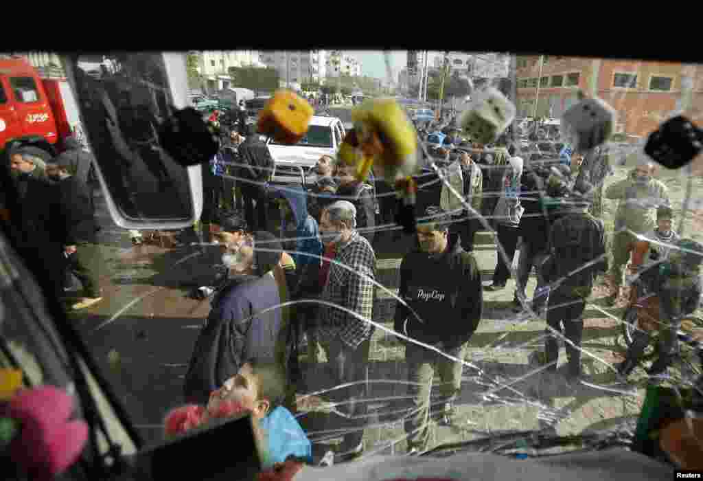 Palestinians are seen through a damaged windscreen of a bus as they gather at the scene of an Israeli airstrike, northern Gaza Strip, Jan. 19, 2014.