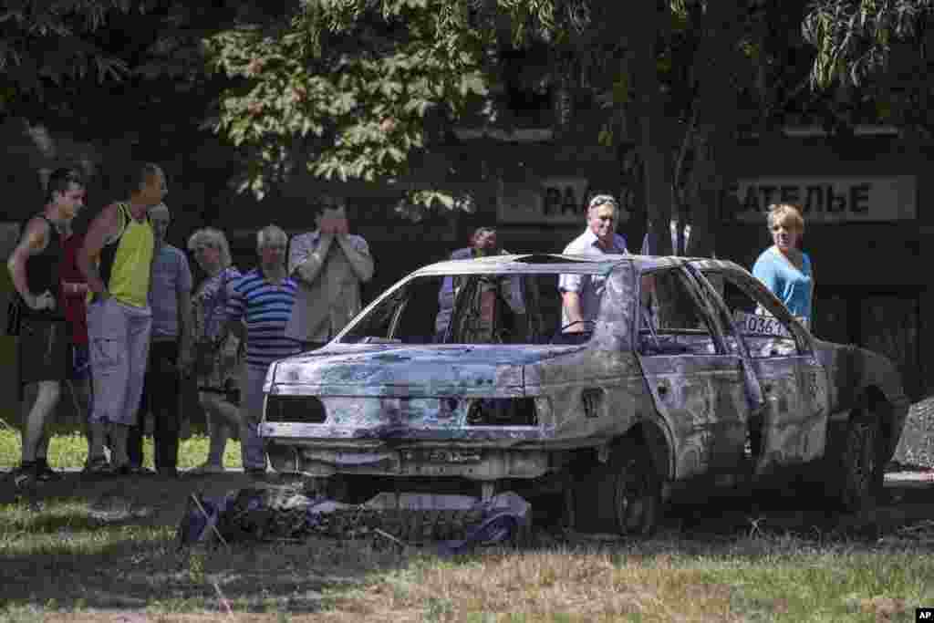 Local people look at a burned out car following a shelling from Ukrainian government forces, in Slovyansk, May 28, 2014.