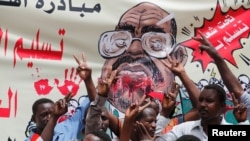 Protesters shout slogans by a banner depicting former Sudanese President Omar al-Bashir, in front of the Defense Ministry in Khartoum, Sudan, April 19, 2019. 